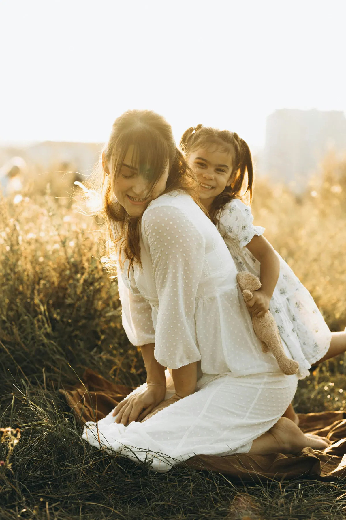 A mother kneeling in long grass with her daughter leaning over her back