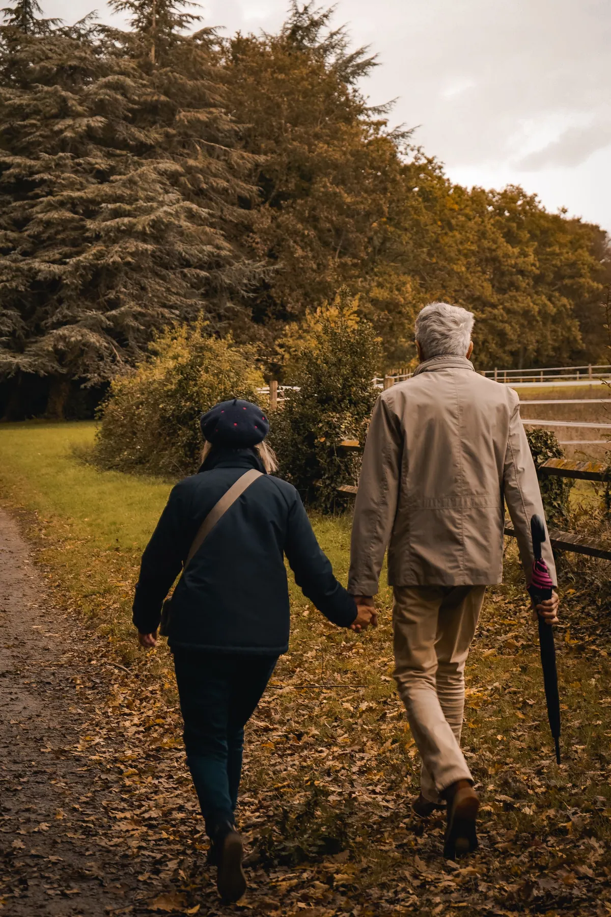 An older couple walking away hand in hand along a path covered in autumn leaves