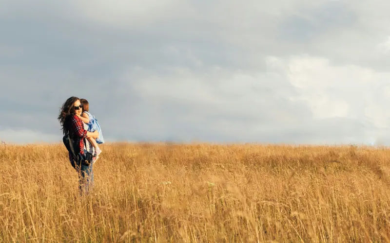 A parent carrying a small child in a wide field beneath an open sky
