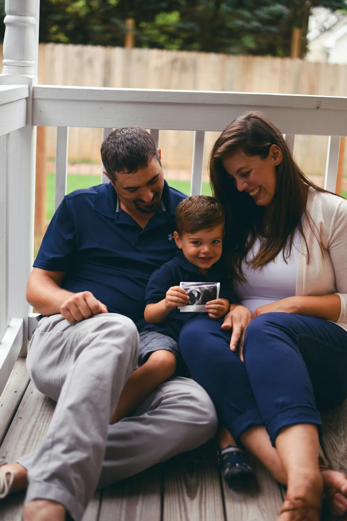 Two parents and a small boy sitting together on a porch step, looking at a photograph