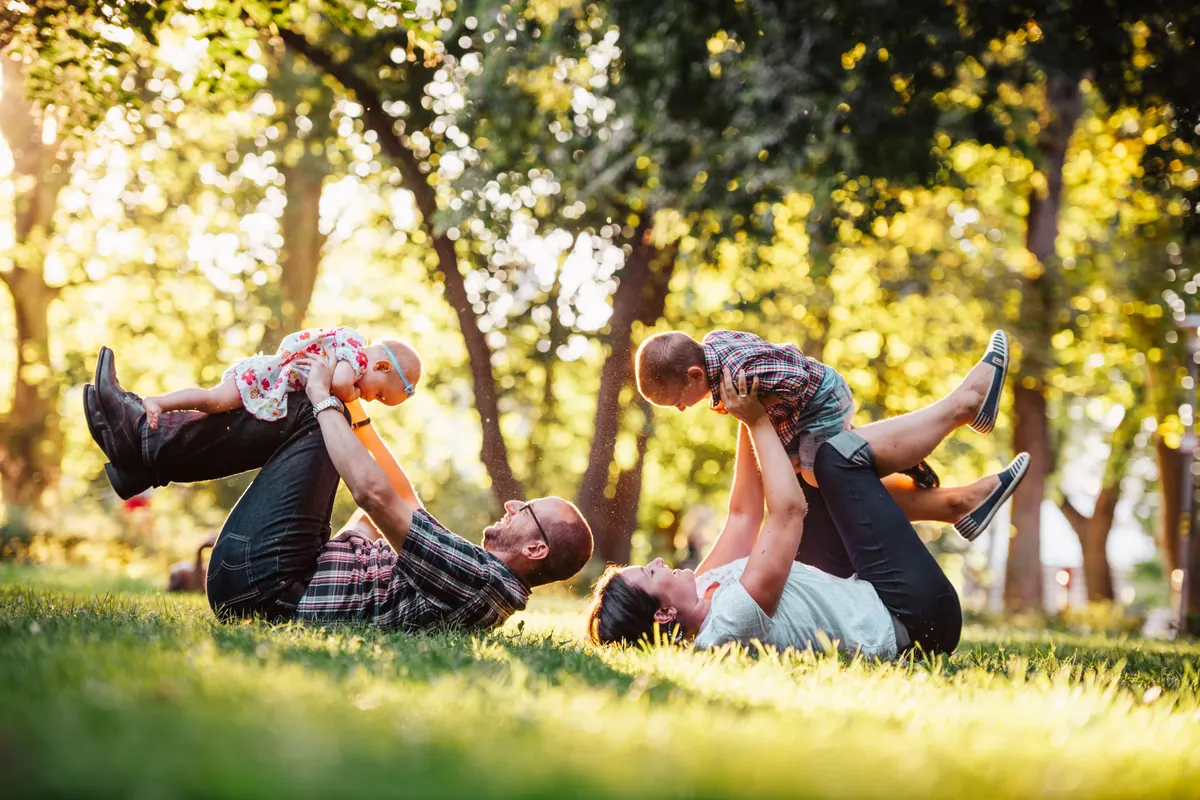 Two adults lying on a lawn lifting two small children above them