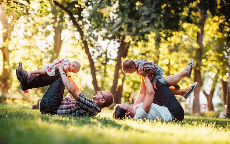Two adults lying on a lawn lifting two small children above them