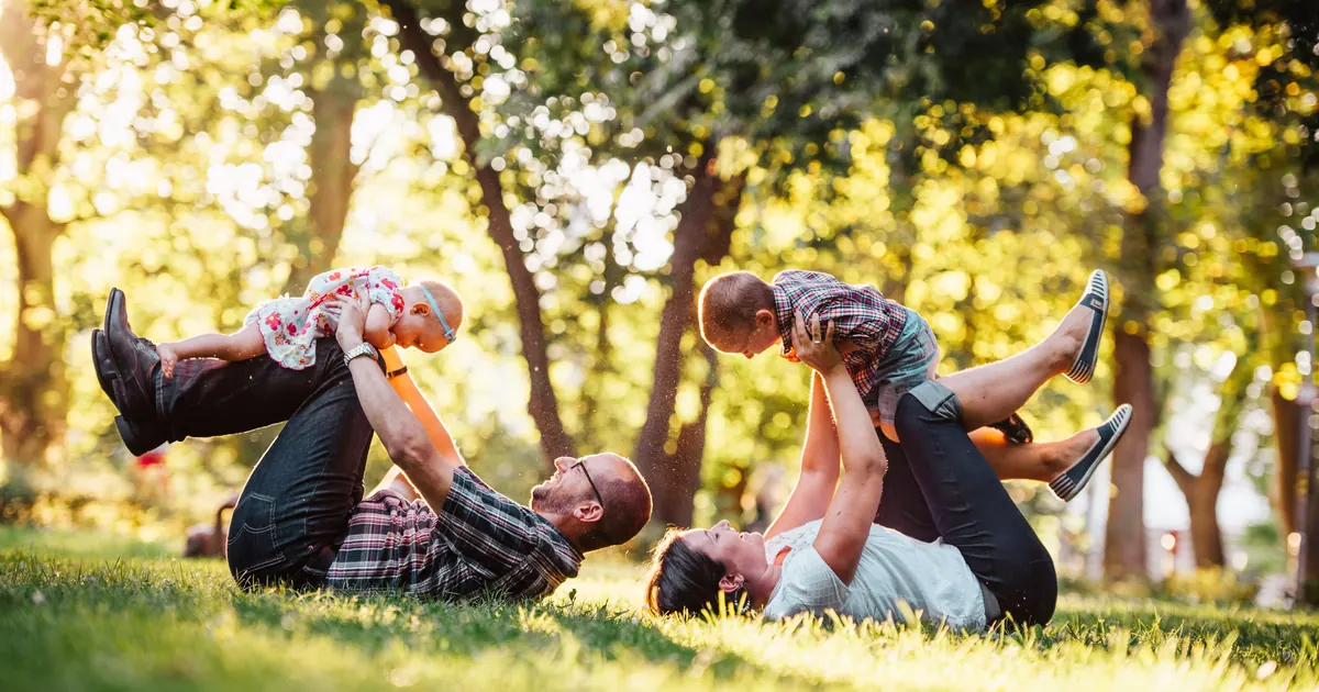 Two adults lying on a lawn lifting two small children above them