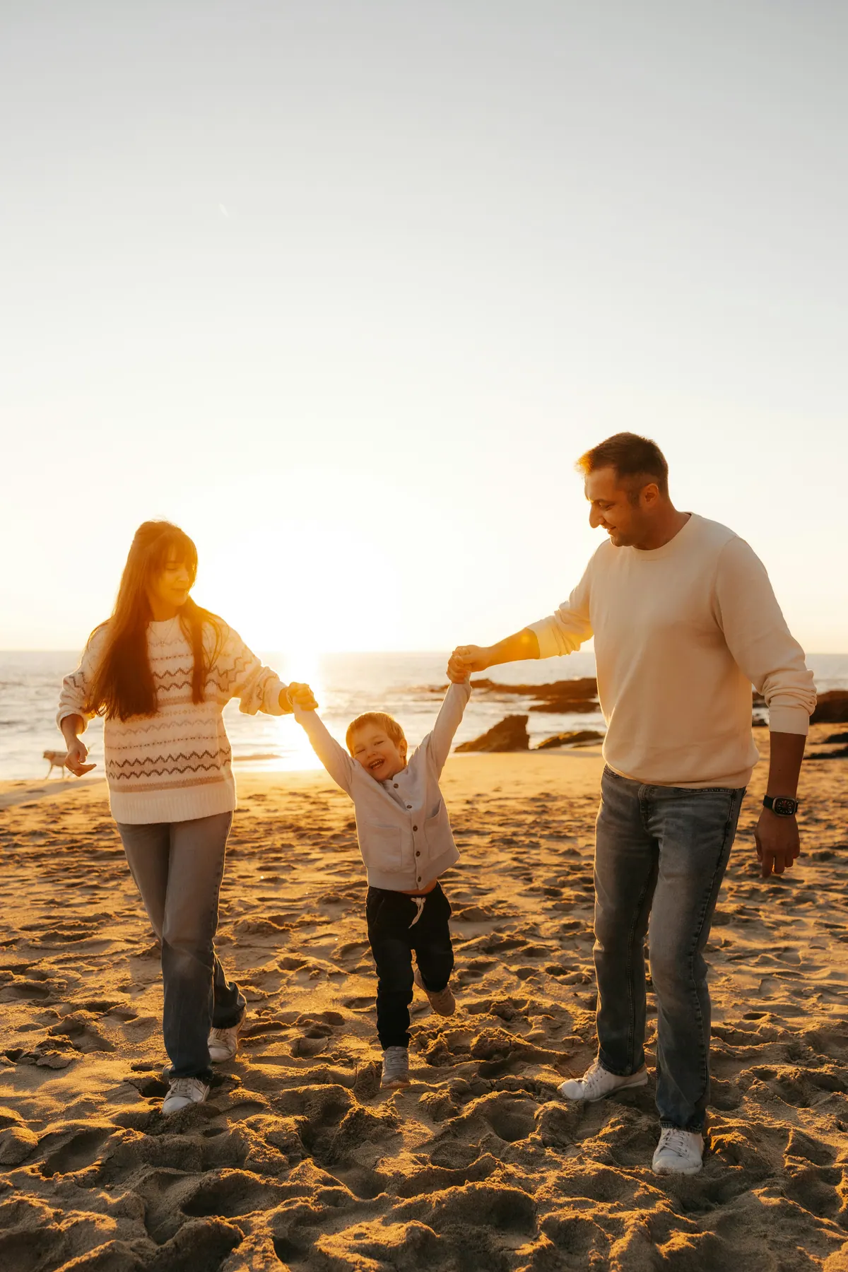 Two parents swinging a small child between them by the hands on a beach at sunset