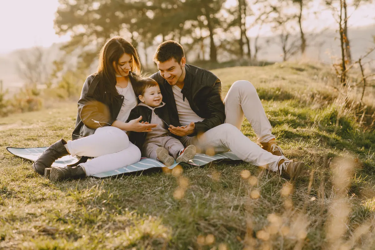 Two parents sitting on a blanket on a hillside with their baby between them