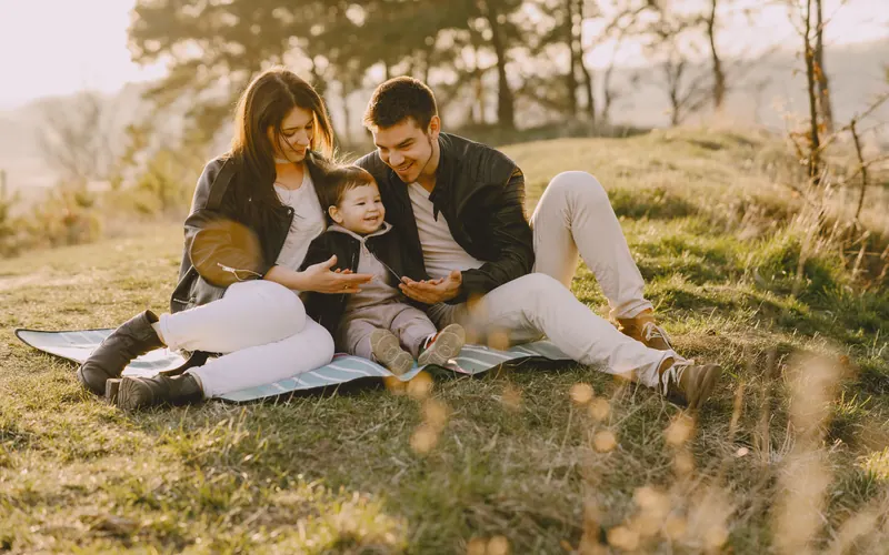 Two parents sitting on a blanket on a hillside with their baby between them