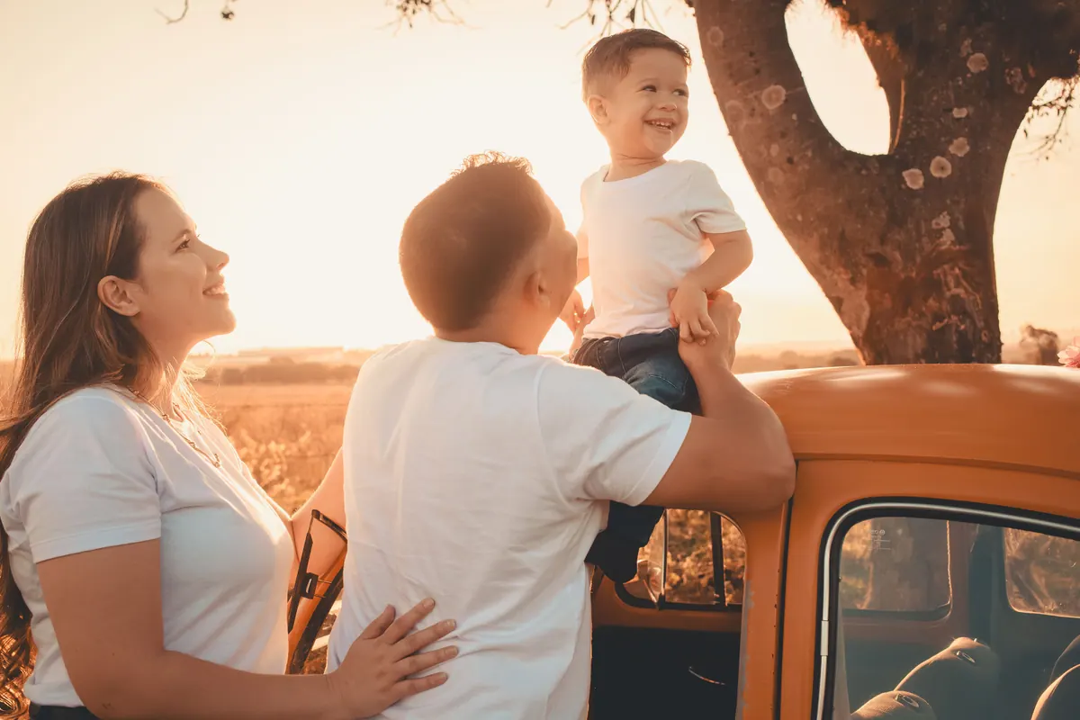 A mother, father and small boy beside an orange pickup truck in a field at sunset
