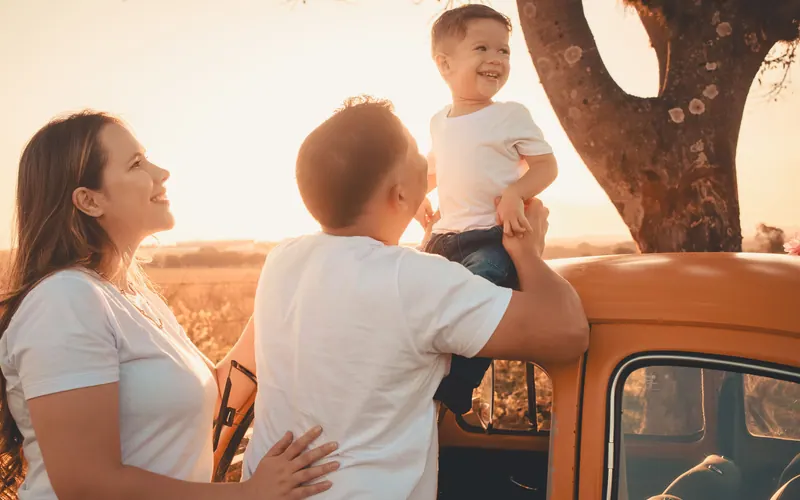 A mother, father and small boy beside an orange pickup truck in a field at sunset