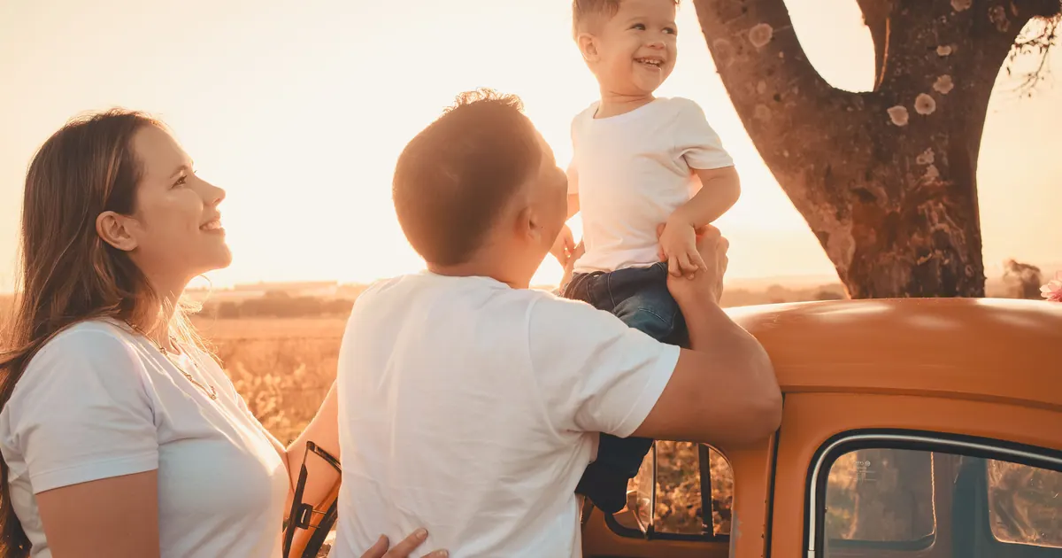 A mother, father and small boy beside an orange pickup truck in a field at sunset